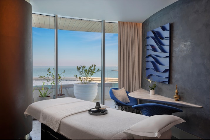 Spa treatment room with a massage table, ocean view, and modern decor.