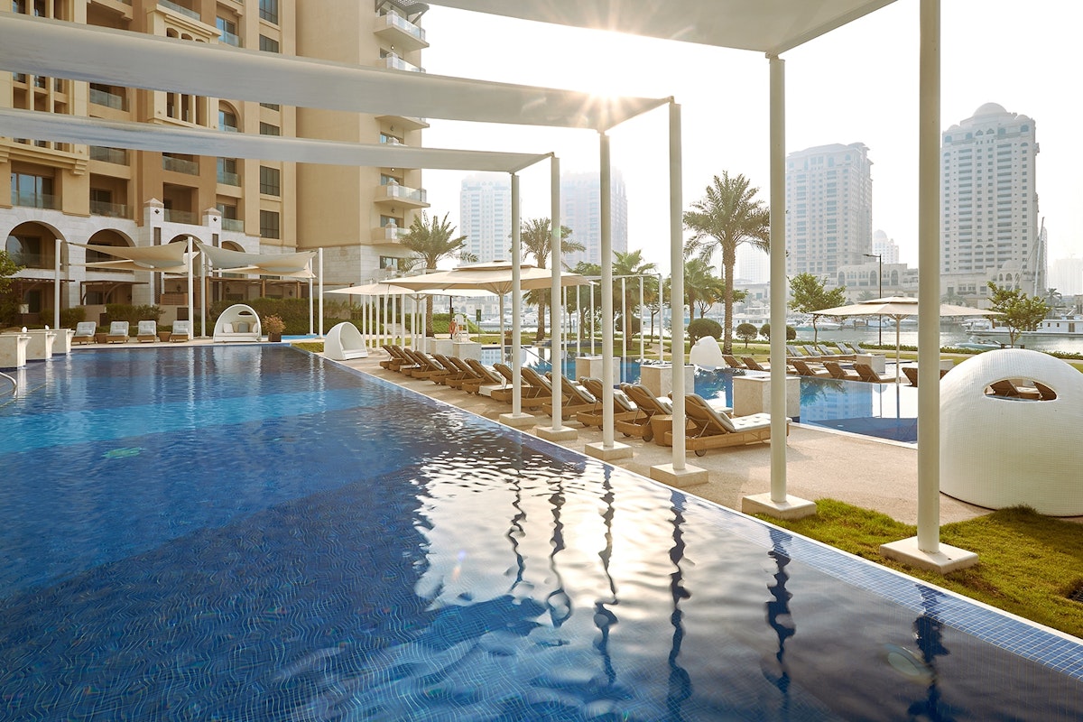 The St. Regis Marsa Arabia Island, The Pearl Qatar Swimming pool with lounge chairs and modern architecture in the background.