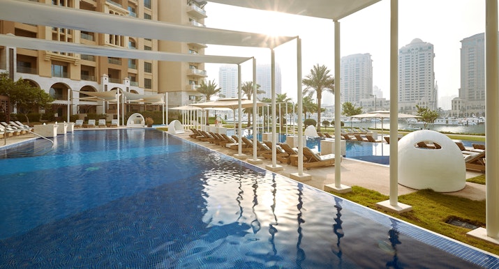 The St. Regis Marsa Arabia Island, The Pearl Qatar Swimming pool with lounge chairs and modern architecture in the background.