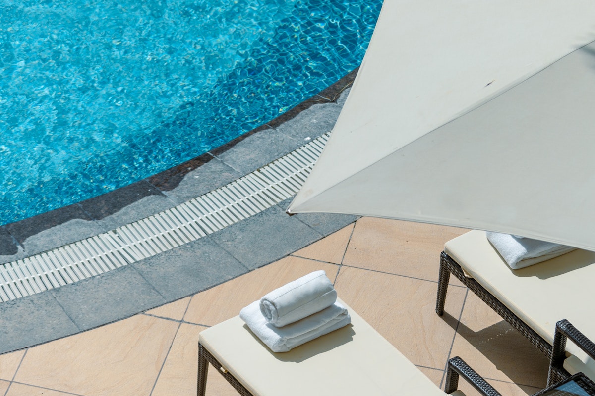A poolside scene with sunbeds, towels, and a parasol.