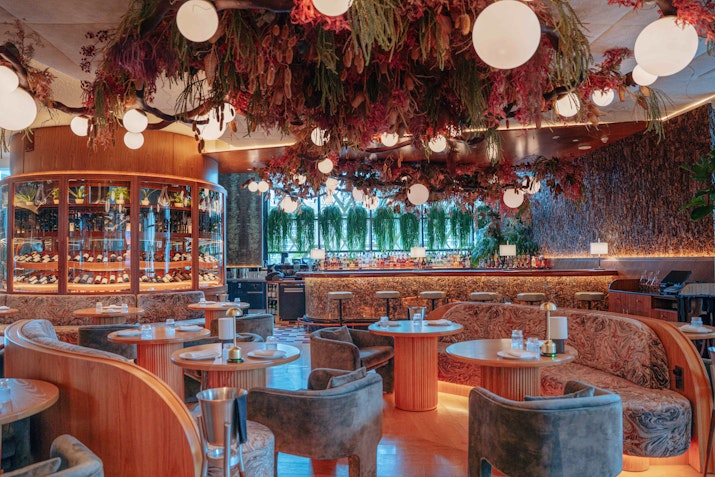 Elegant restaurant interior with lush hanging plants, round tables, and soft lighting.