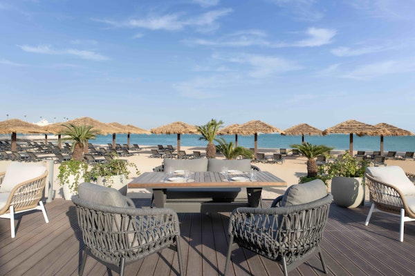 Outdoor lounge area with wicker chairs, a table, and umbrellas by the beach.