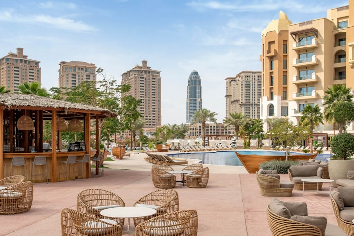 Outdoor lounge area with wicker furniture and a bar overlooking the pool and buildings.