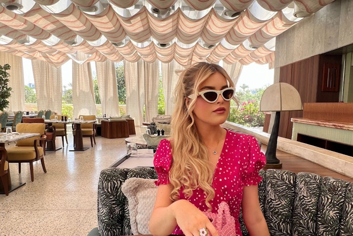 Young woman in sunglasses sitting in a stylish restaurant with a patterned ceiling and elegant decor.