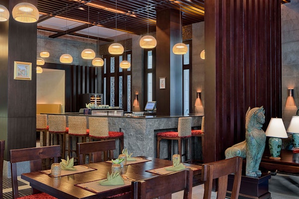 The Westin Doha Hotel & Spa Cozy restaurant interior with wooden tables, a bar, and ambient lighting