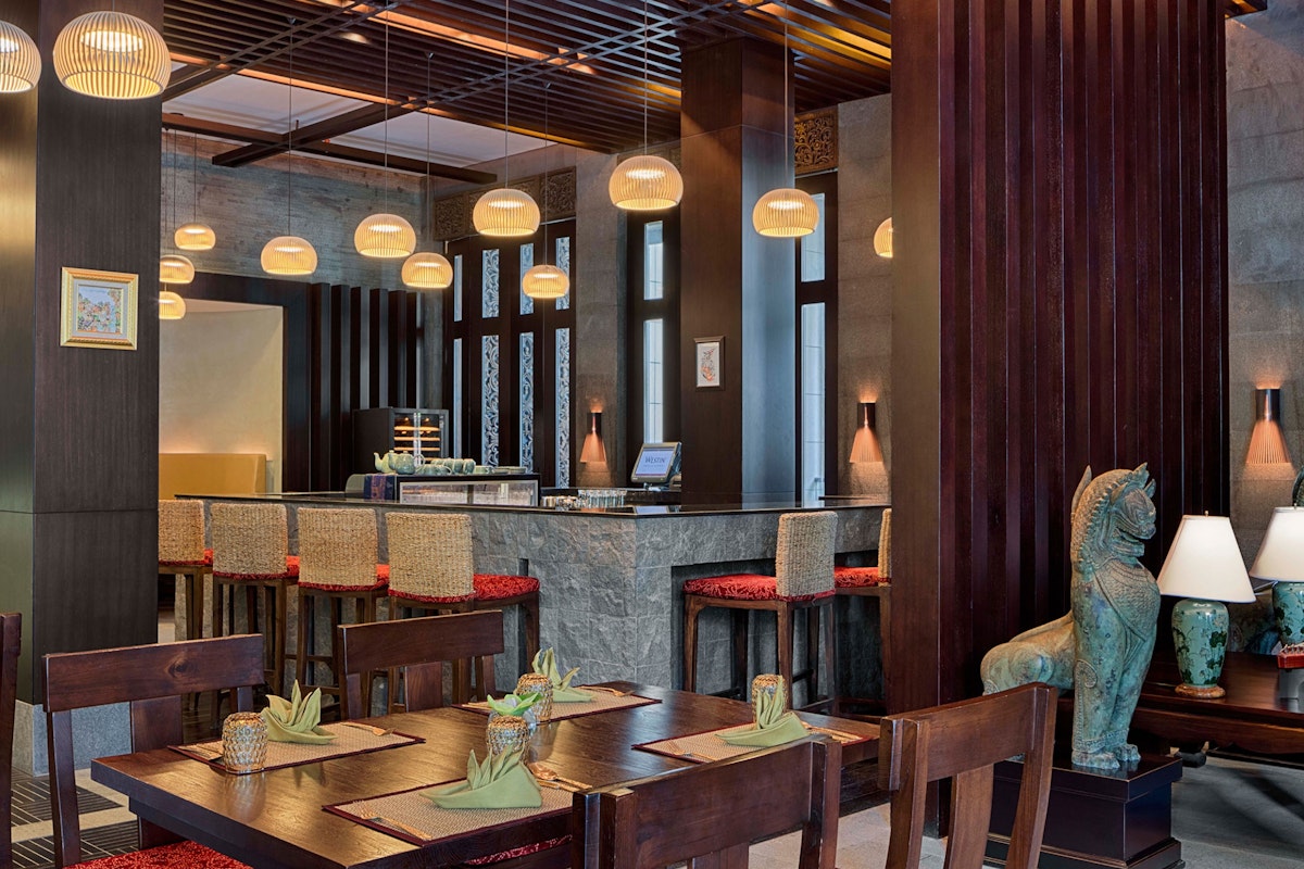 The Westin Doha Hotel & Spa Cozy restaurant interior with wooden tables, a bar, and ambient lighting