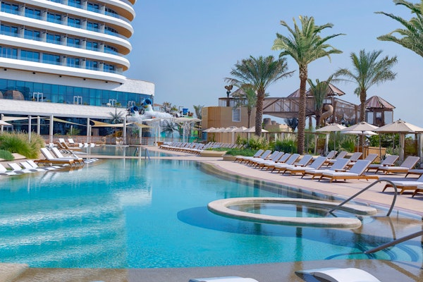 Poolside lounge chairs with water slides and palm trees, featuring a hotel in the background.