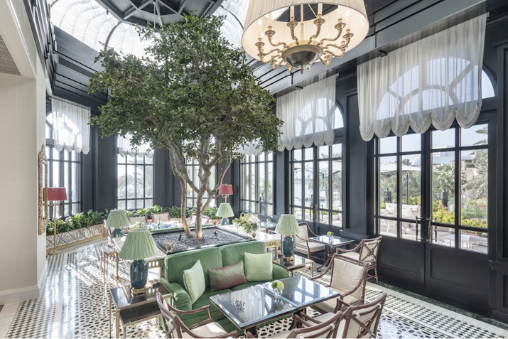 Elegant lounge with a large tree centerpiece, green seating, and natural light from large windows