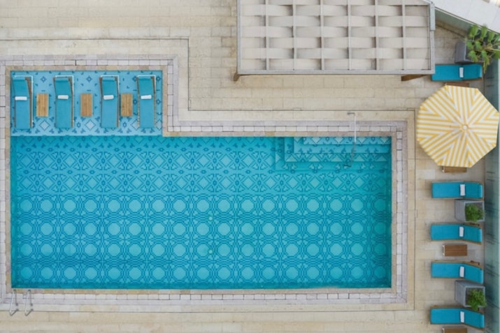 Aerial view of a pool with lounge chairs, umbrellas, and patterned tiles.