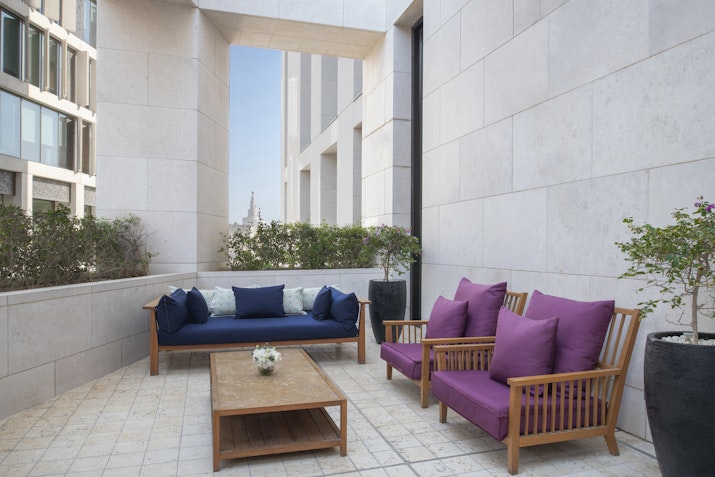 Outdoor seating area with purple and blue cushions, surrounded by walls and plants.