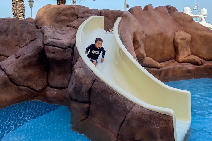 Child sliding down a water slide into a pool with rocky surroundings