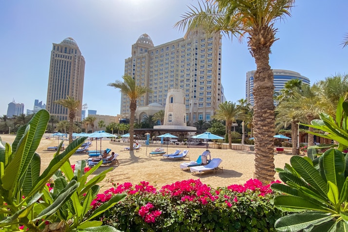 Resort beach with lounge chairs, palm trees, and a hotel in the background