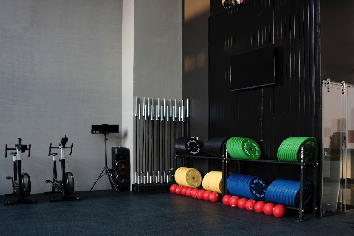 Two exercise bikes beside colorful weighted balls and equipment stacked on racks in a gym.