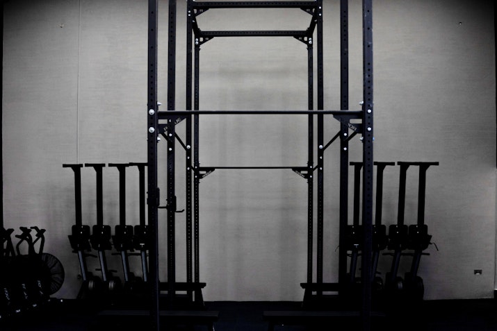 A gym rack with equipment on the floor and a black frame structure for exercises in the background