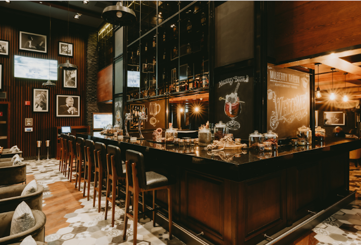 Eat Hilton Doha The Pearl Cozy bar with dark wood decor, bar stools, and a well-stocked liquor shelf, adorned with vintage photos and chalkboard signage.