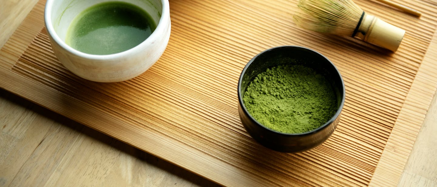 Top view of a bowl with freshly whisked matcha, traditional bamboo whisk, and a container with vibrant green matcha powder.