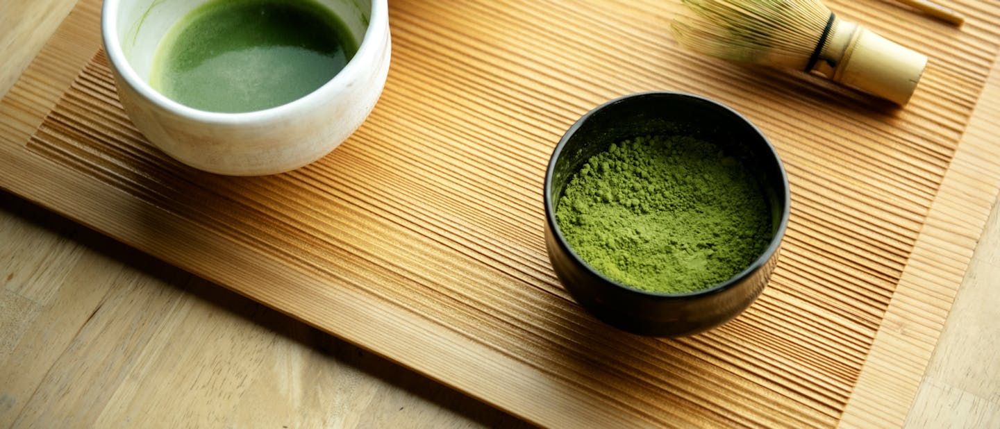 Top view of a bowl with freshly whisked matcha, traditional bamboo whisk, and a container with vibrant green matcha powder.