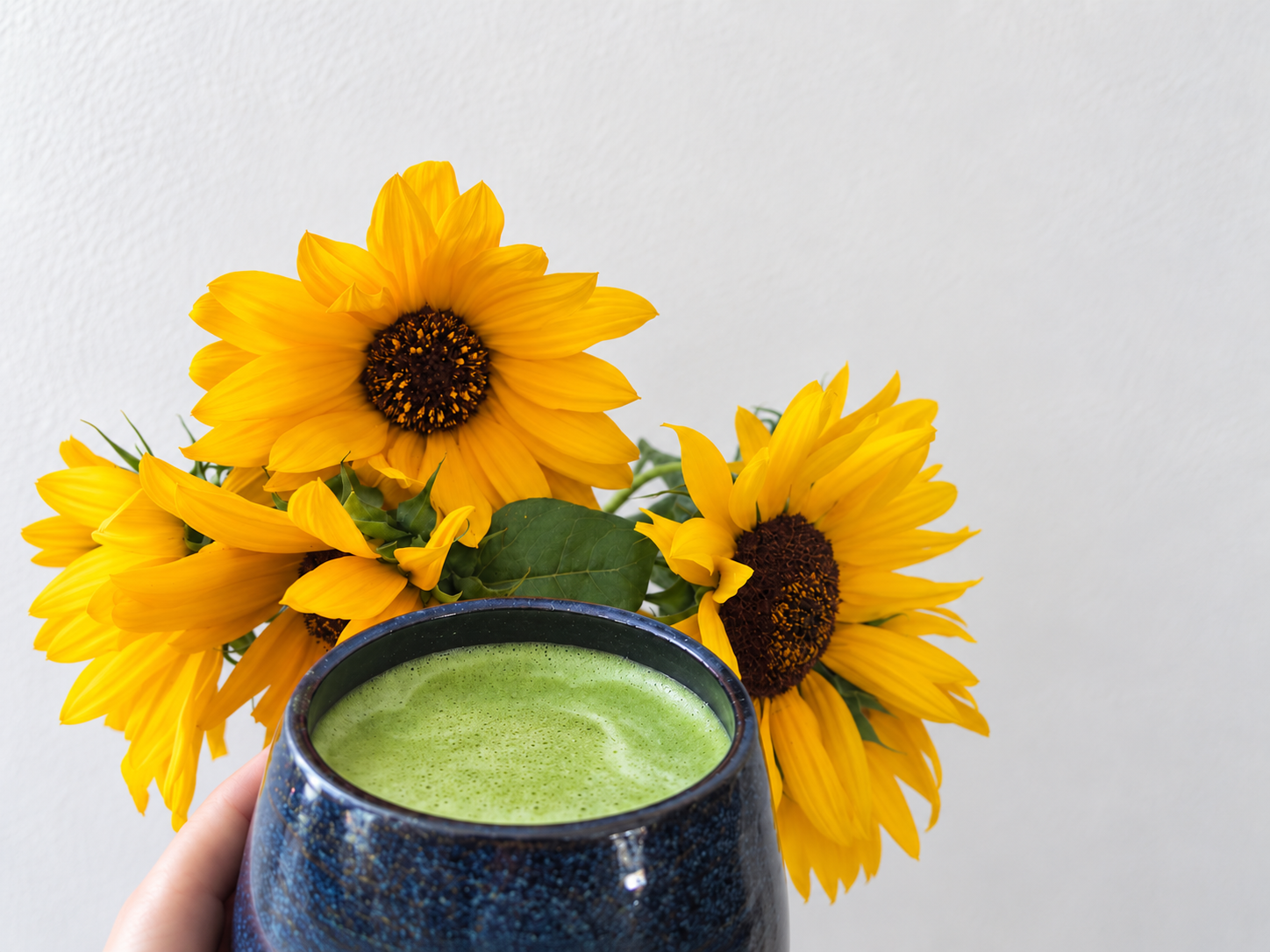 A cup of freshly prepared matcha in front of a bouquet of sunflowers.