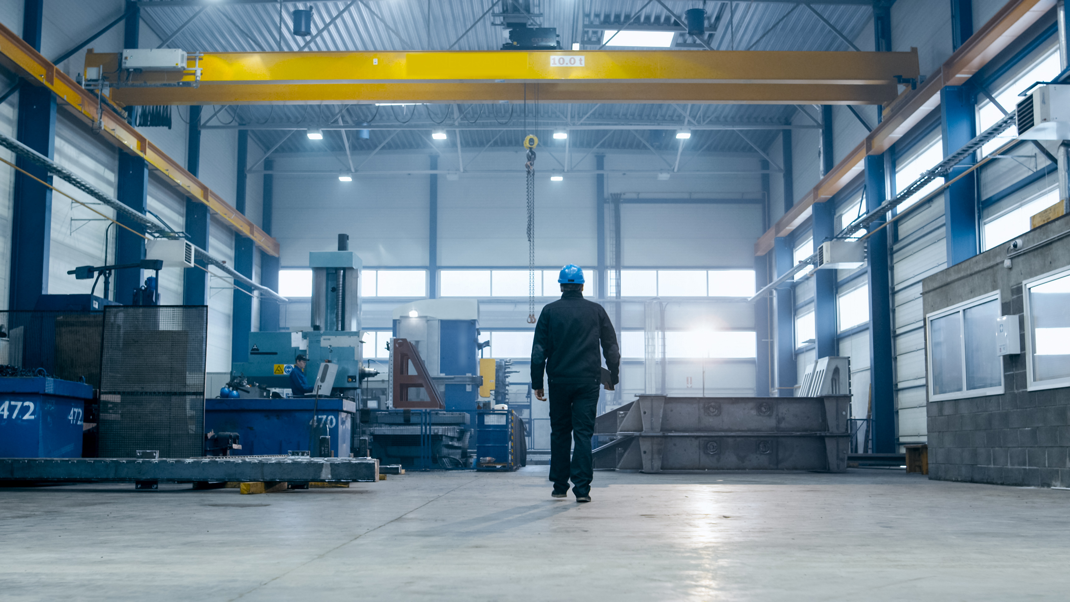 Un operaio che indossa un elmetto cammina all'interno di un grande impianto industriale.