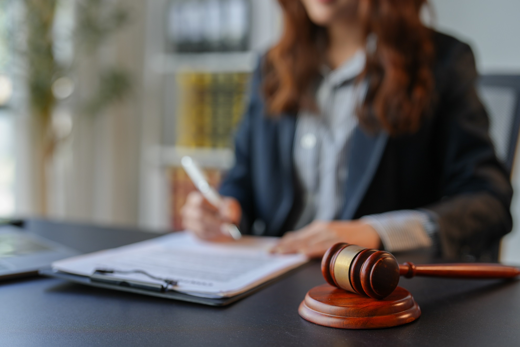 A professional woman in business attire writing on paper, with an auction gavel and a laptop on the desk, symbolizing the connection between banking and online auctions.