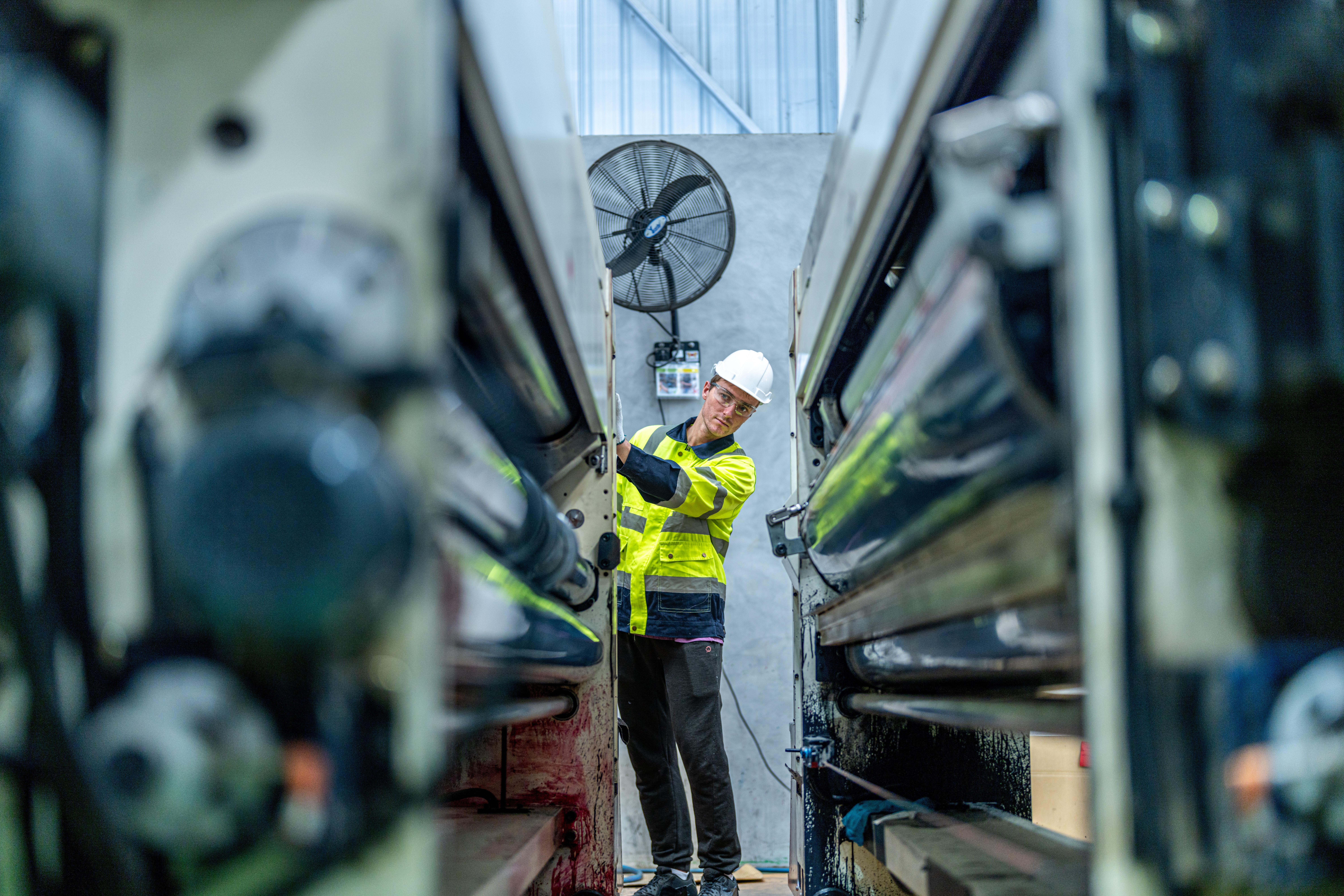 An industrial engineer inspecting machine components inside a factory, representing operations and system checks in a heavy manufacturing environment.