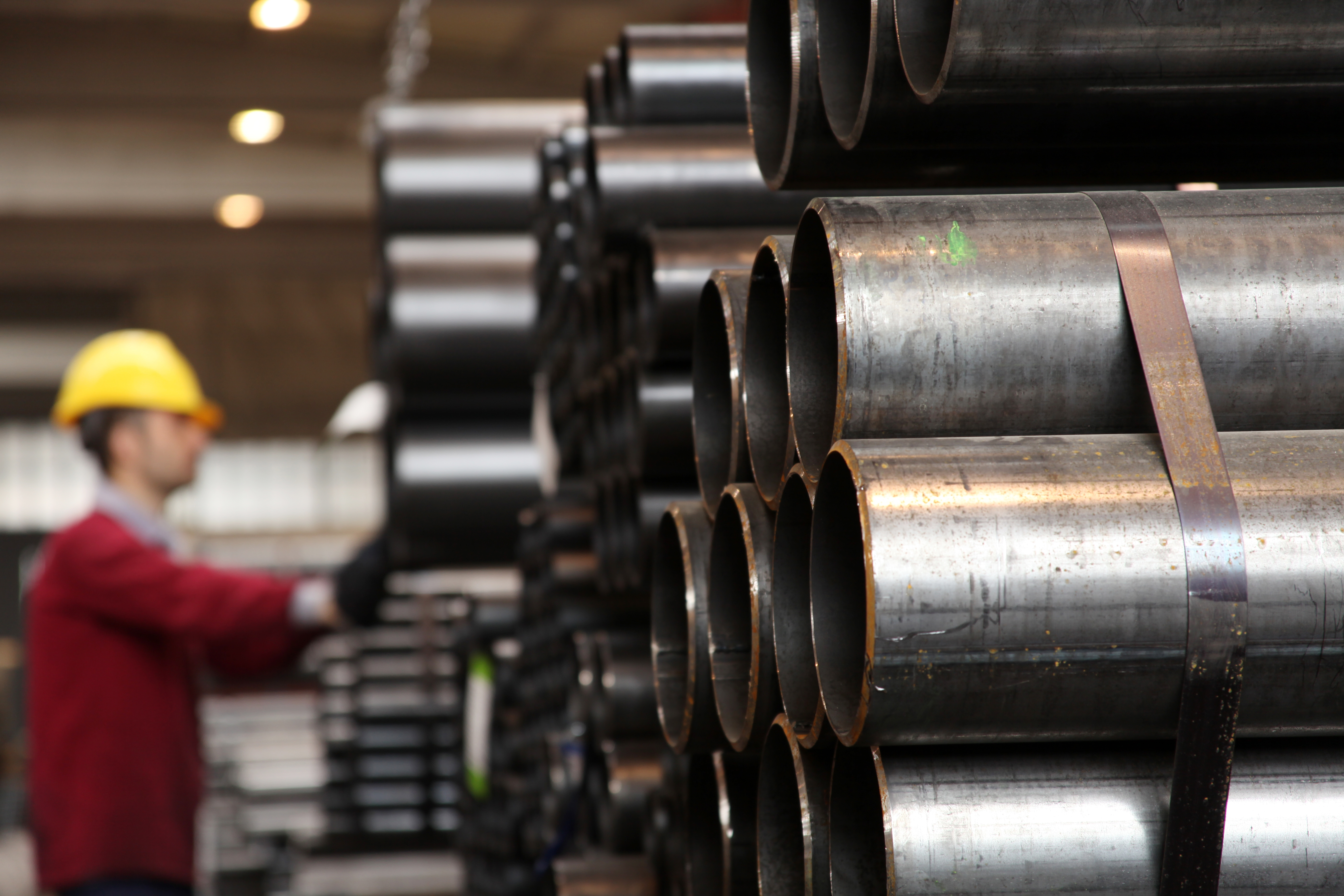 A factory worker inspecting stacked pipes, emphasizing the importance of quality control in industrial manufacturing.