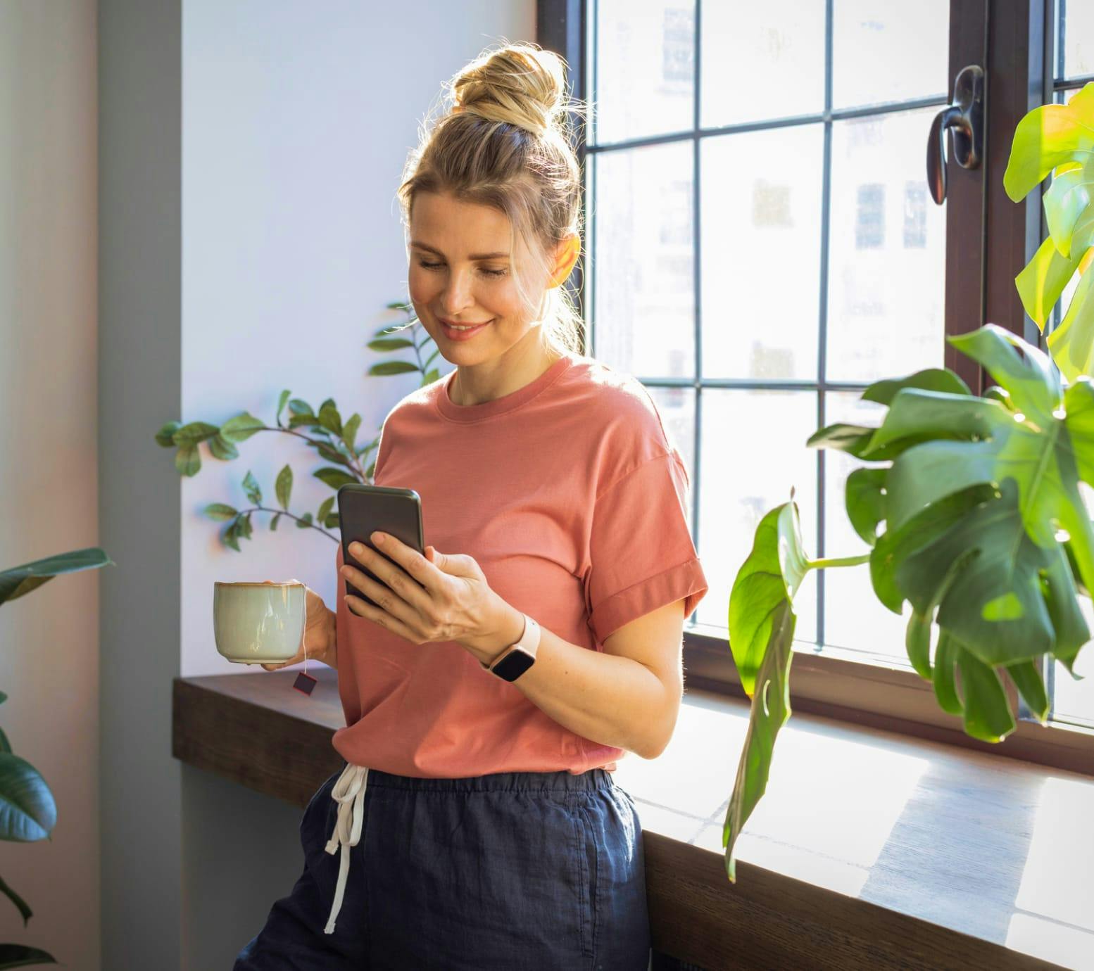 Woman standing by a window, looking at her phone