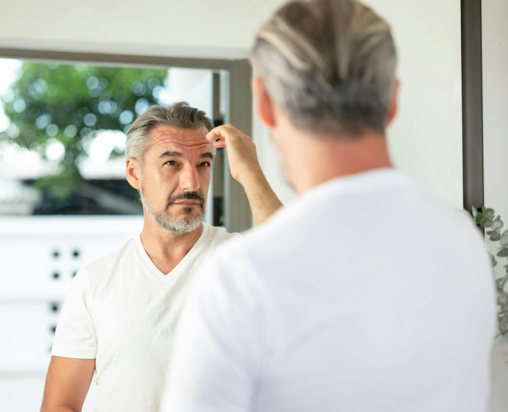 man with grey hair looking into a mirror