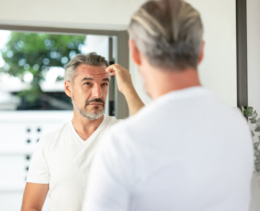 man with grey hair looking into a mirror