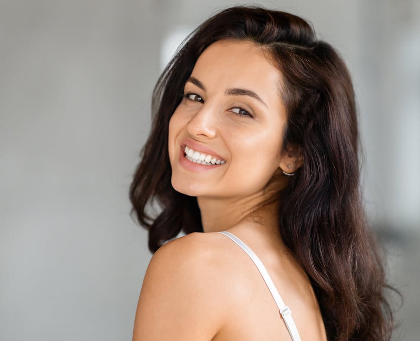 woman with long dark brown hair smiling over her shoulder