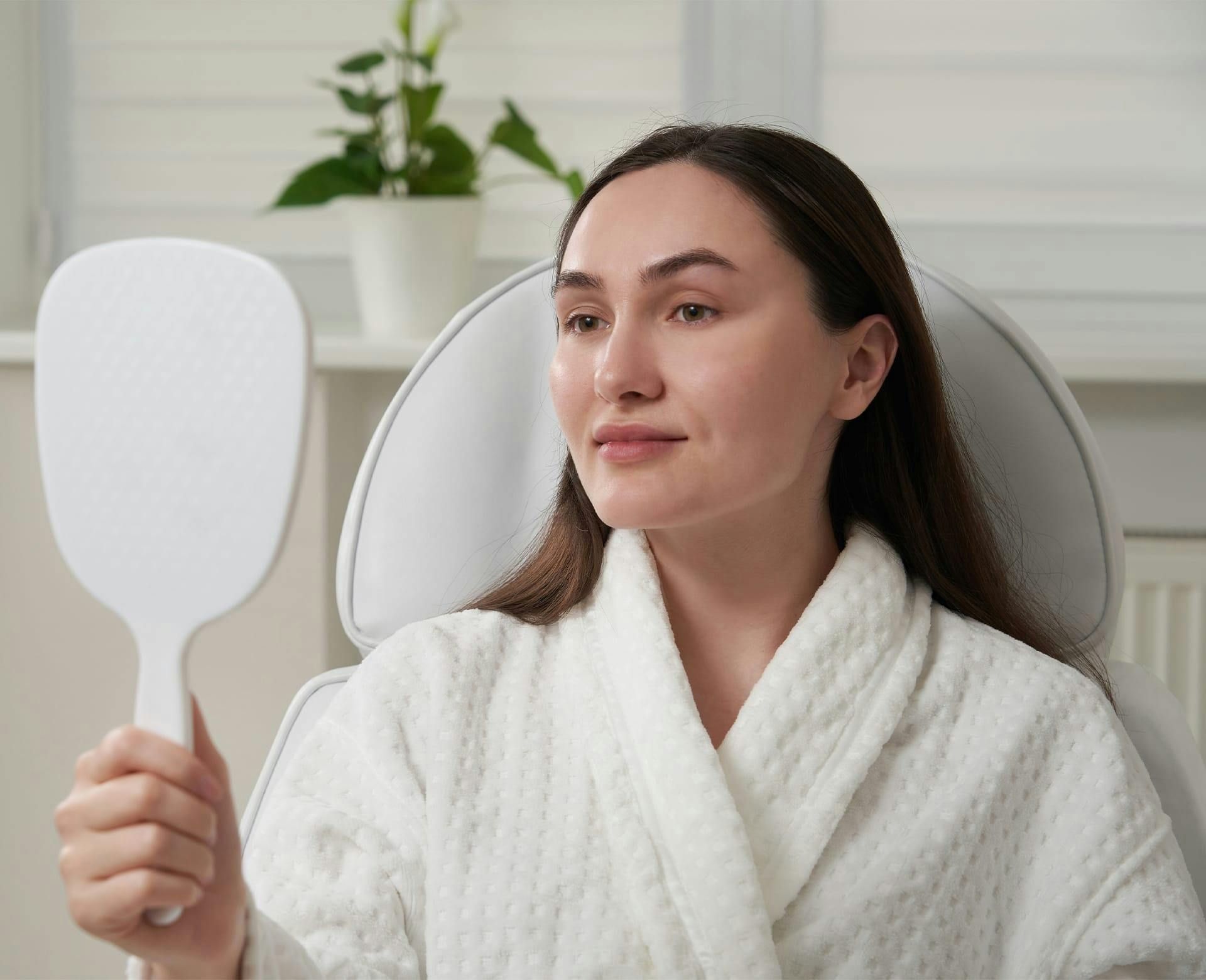 woman in a robe looking at herself in a handheld mirror