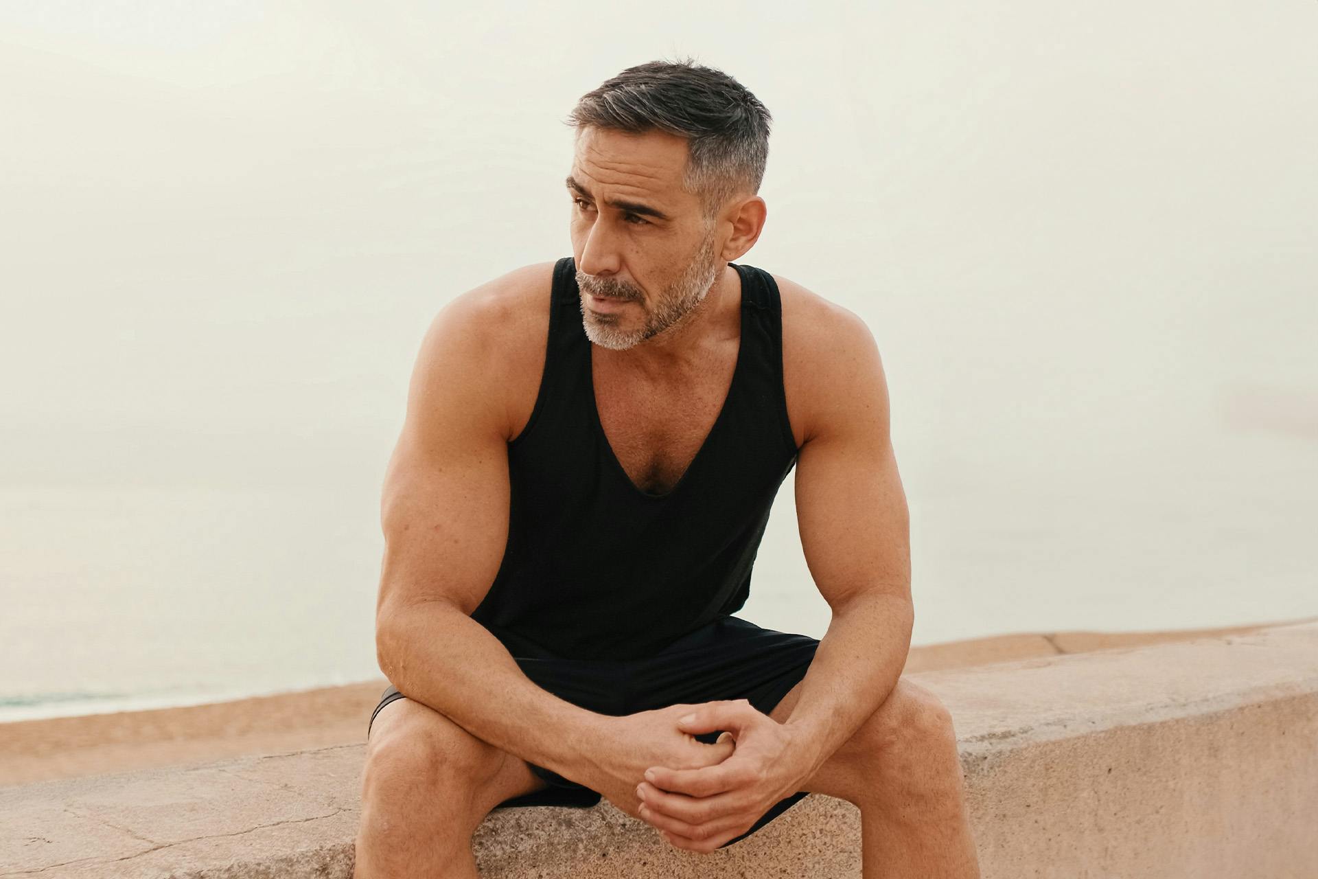 man in a black tank top and shorts sitting down