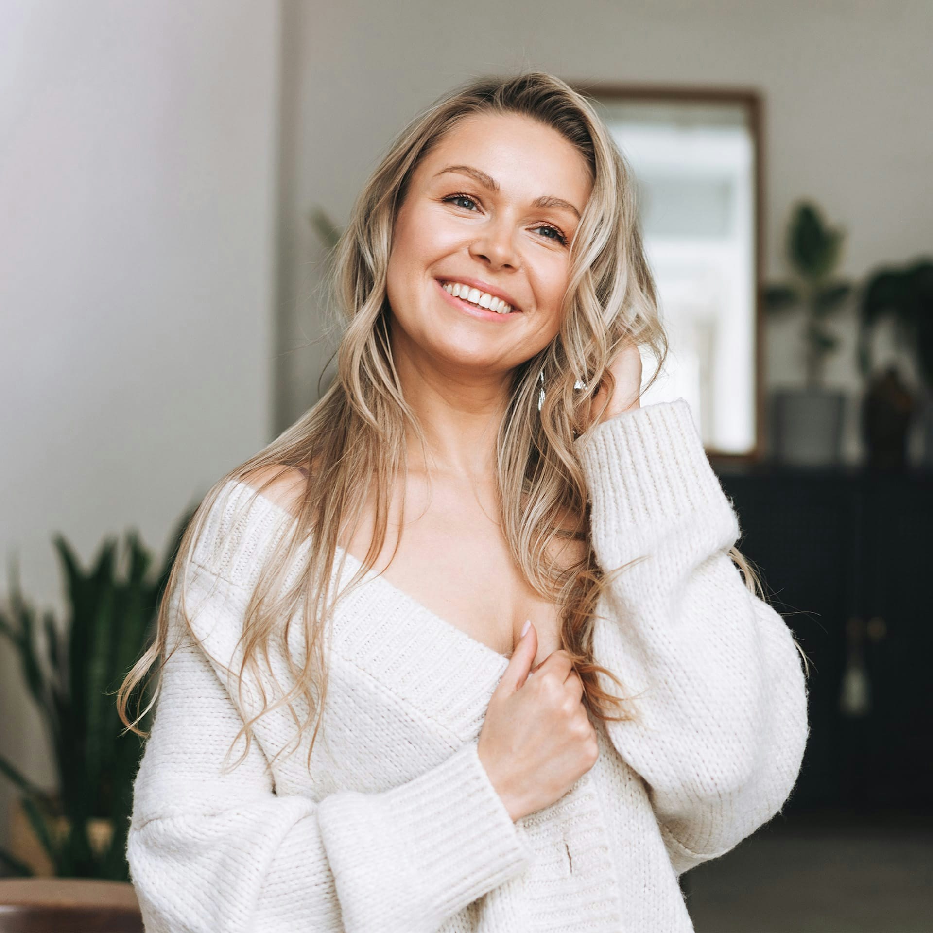woman with blonde hair smiling and wearing a white sweater