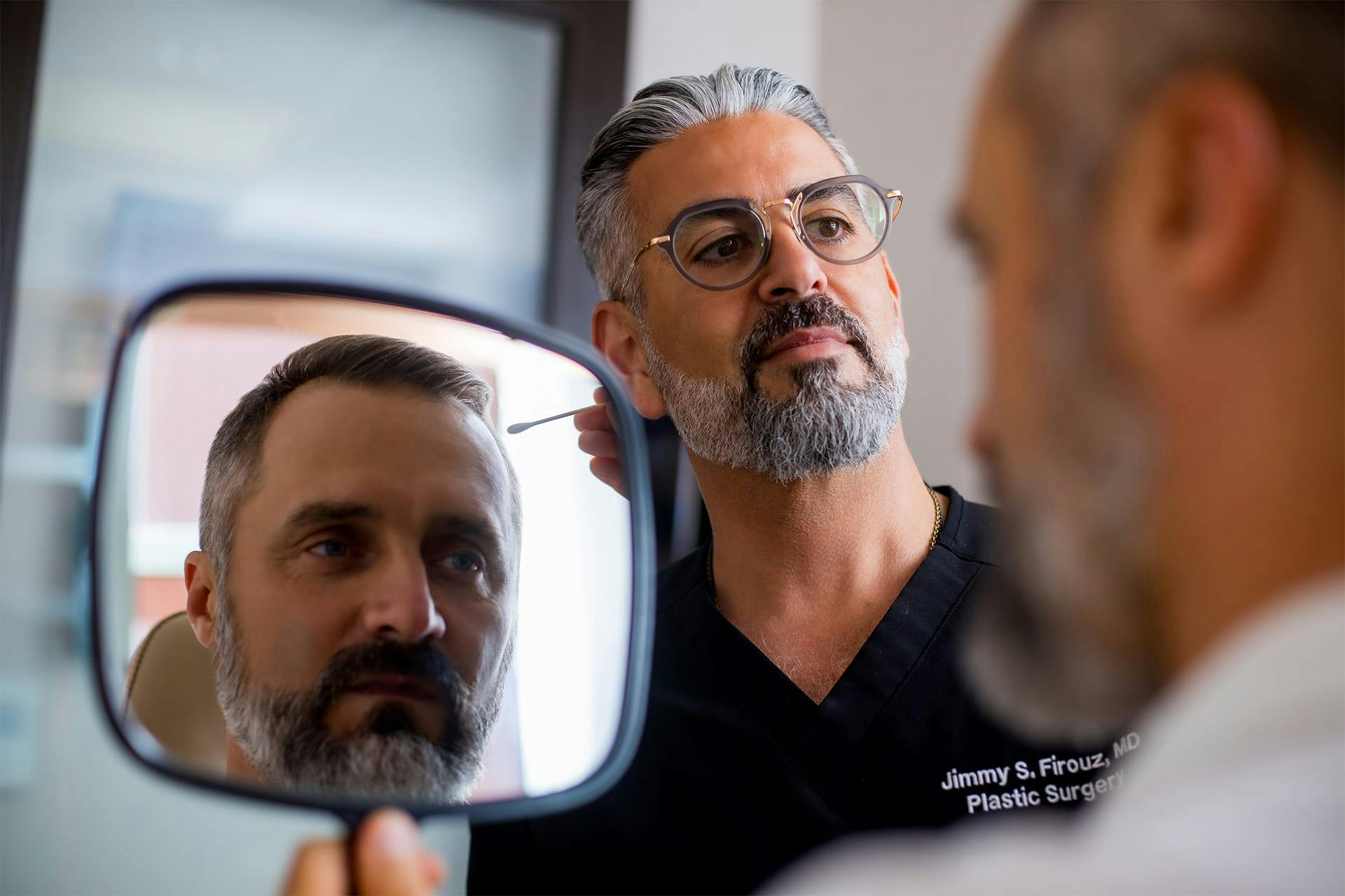 Dr. Firouz showing a male patient his results in a handheld mirror