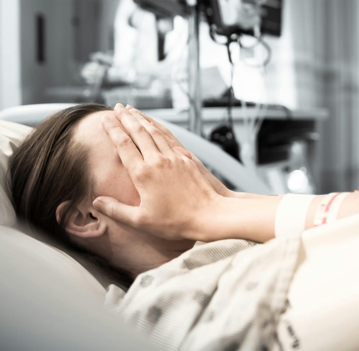 woman in hospital bed with face in her hands