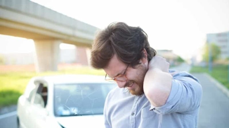 Man holding his neck while standing in front of a car