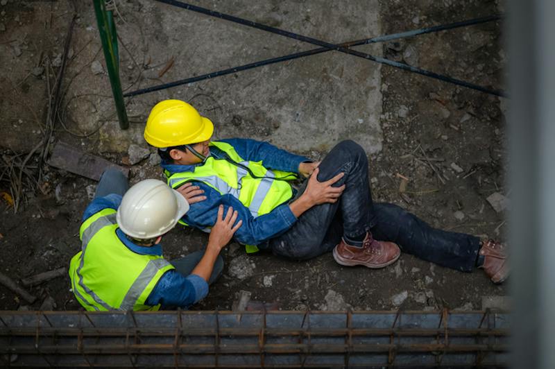 A worker with an injured leg laying on ground