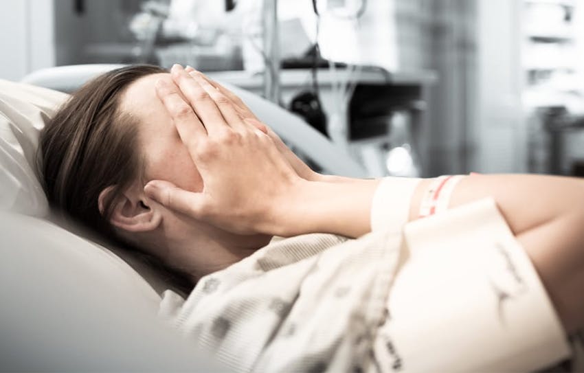 woman in hospital bed with hands on her face
