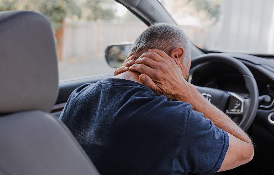 man in car holding his neck in pain