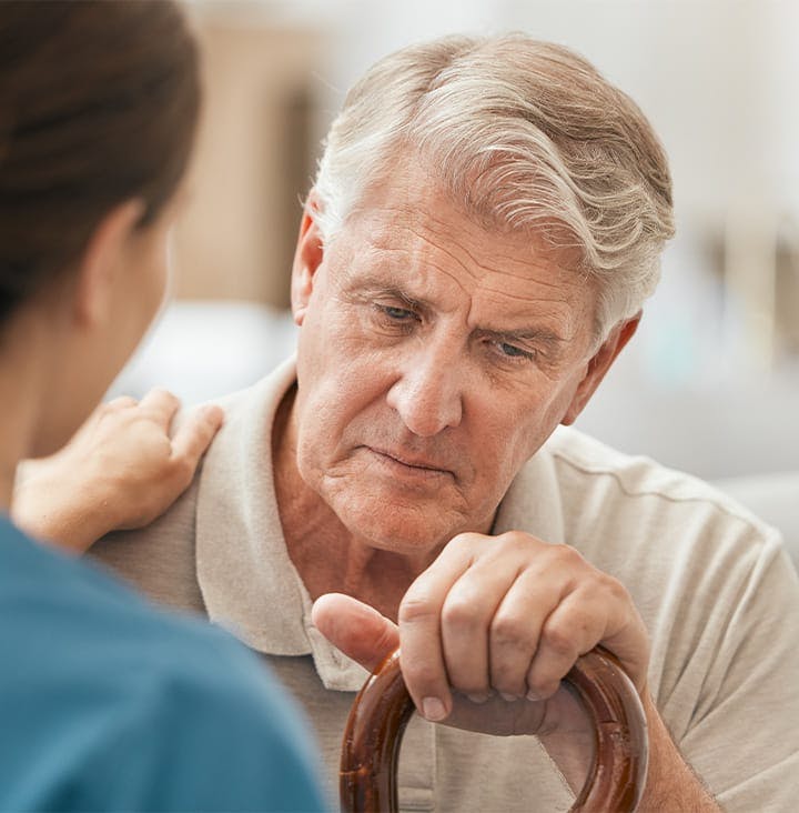 older man looking upset with nurse's hand on his shoulder