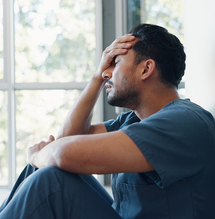 man sitting near window with palm on his forehead