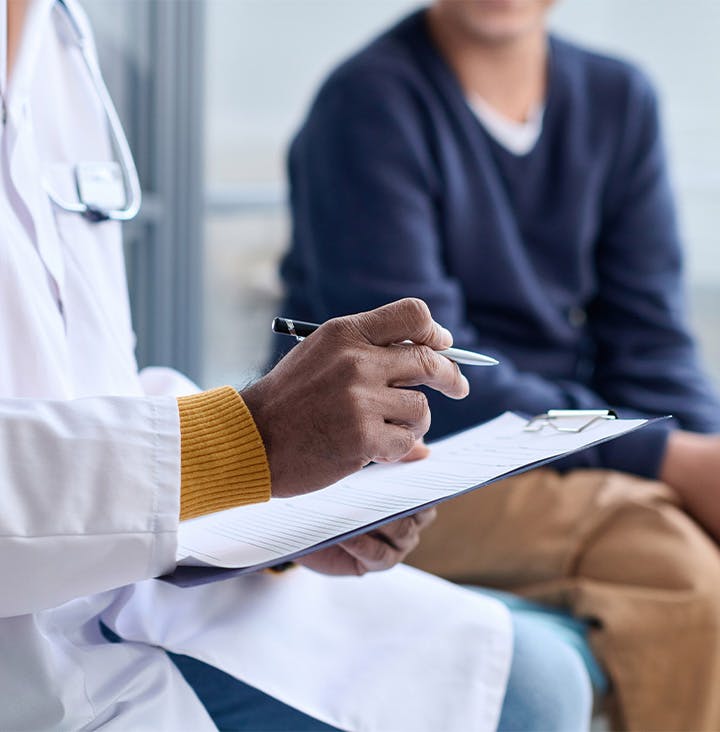 doctor writing on clipboard with patient in the background