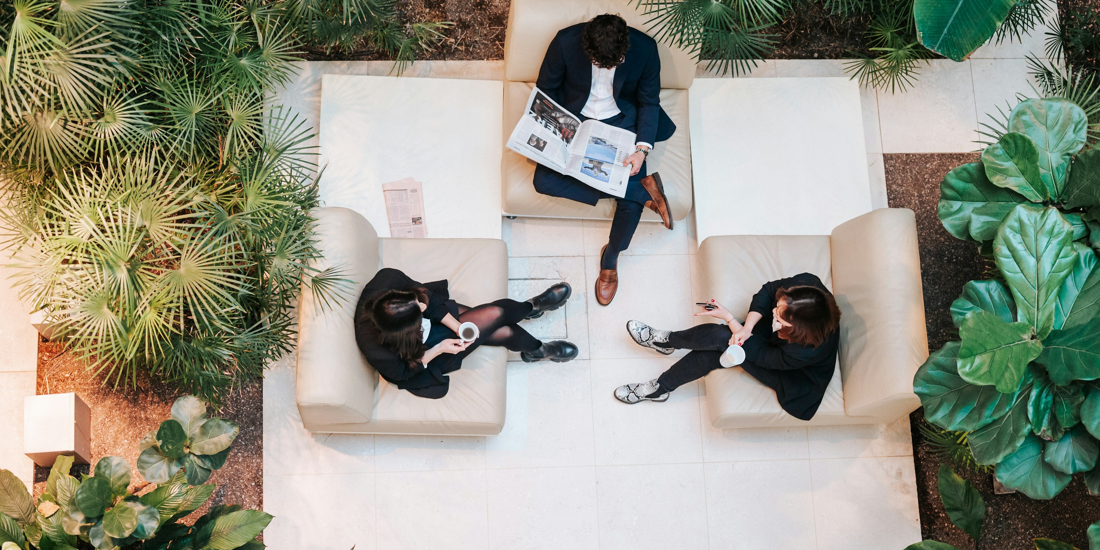 Drei Mitarbeitende der Baaderbank sitzen im begrünten Lounge-Bereich mit Zeitung und Kaffeetassen.