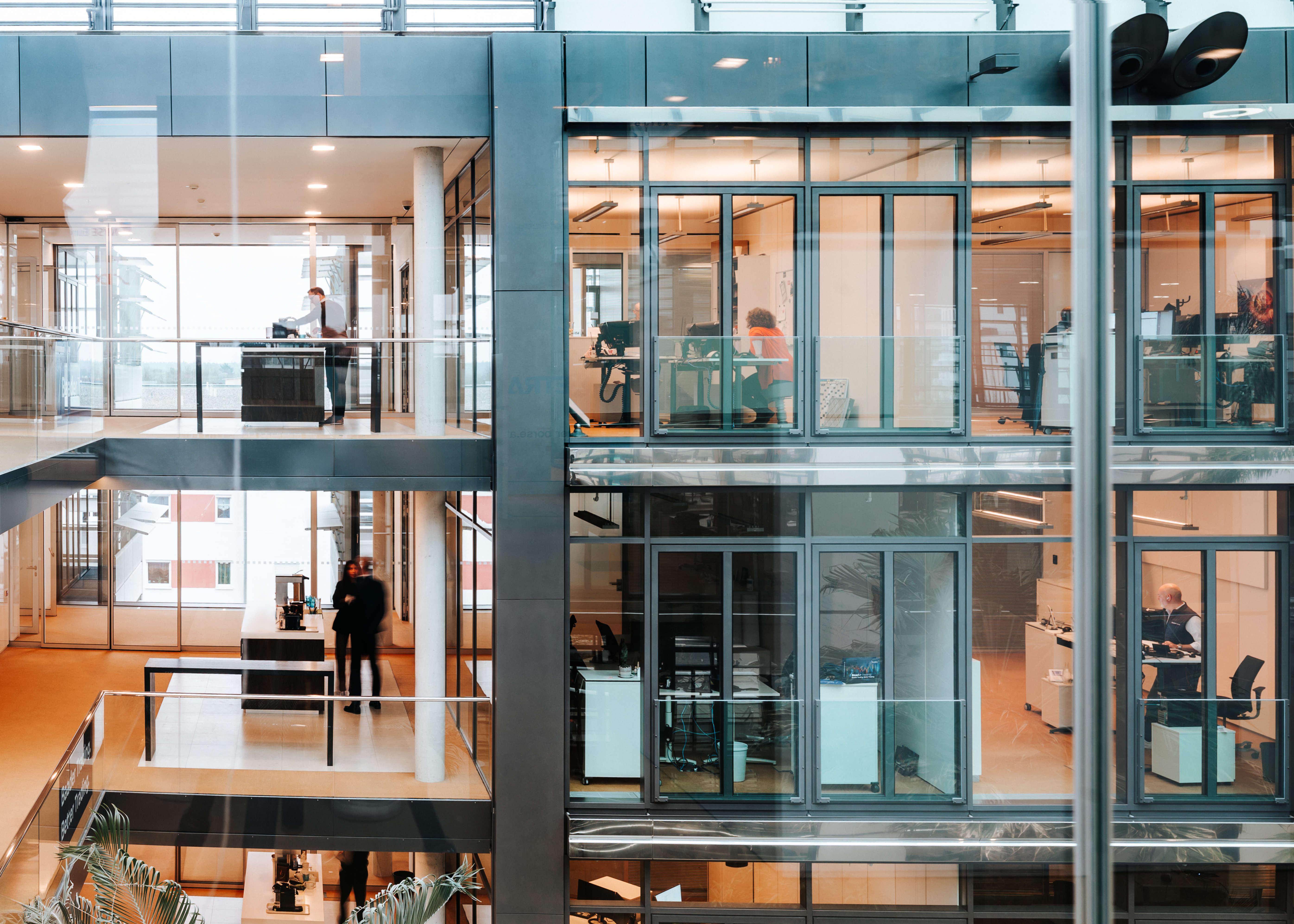 Innenansicht des modernen Baaderbank Bürogebäudes mit Glasfronten und Mitarbeitenden an Schreibtischen.