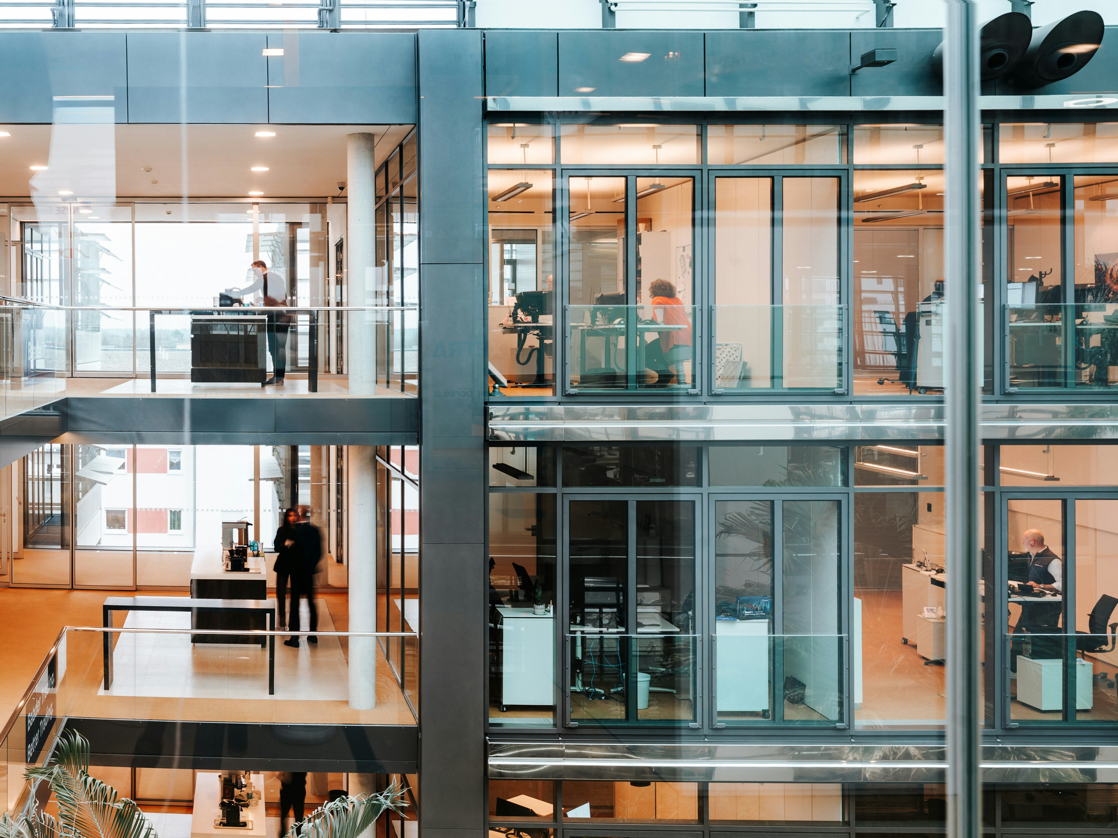 Innenansicht des modernen Baaderbank Bürogebäudes mit Glasfronten und Mitarbeitenden an Schreibtischen.
