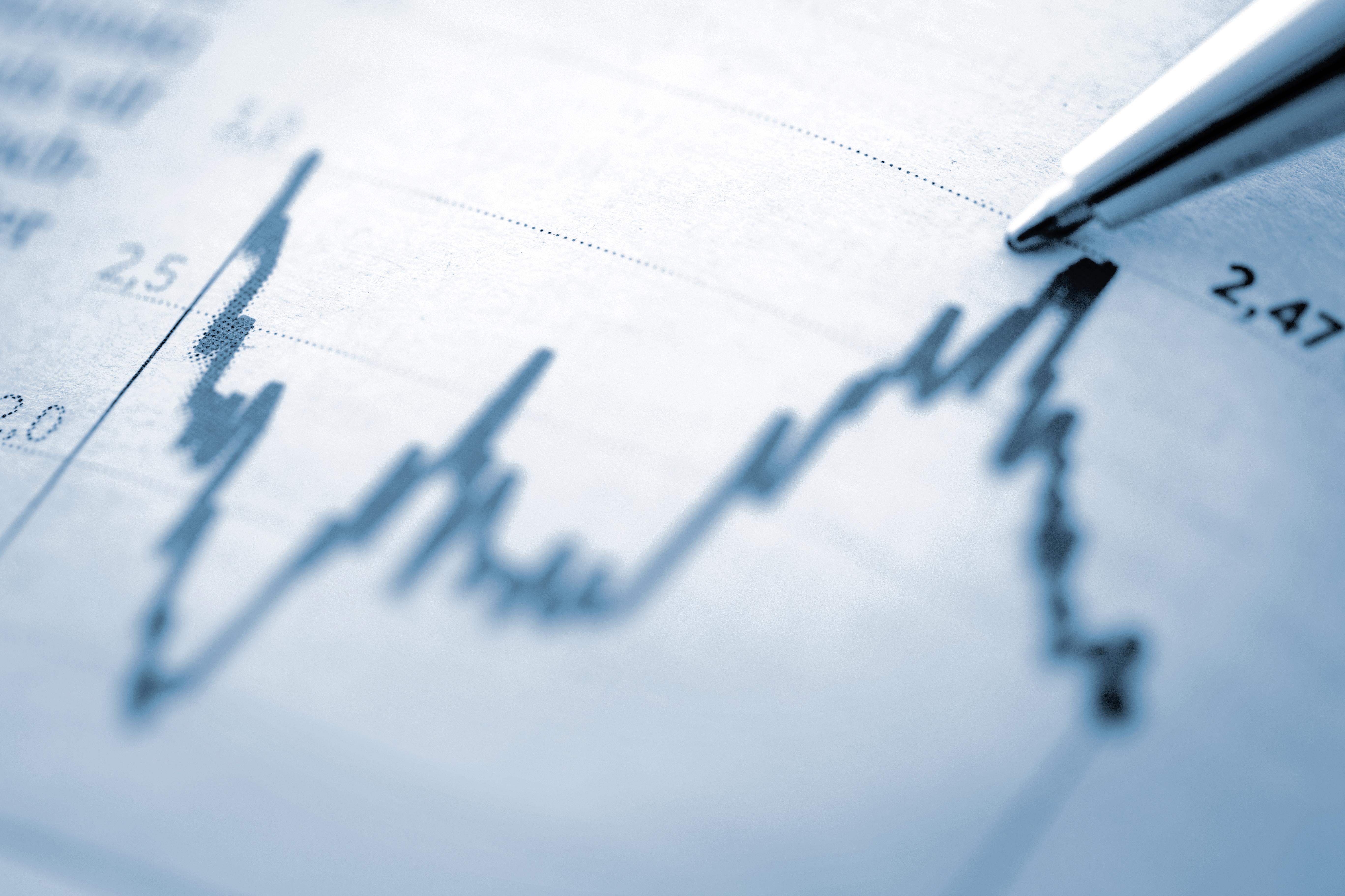 Nahaufnahme einer Finanzgrafik mit schwankender Kurslinie und einem Kugelschreiber, der auf den Verlauf im Diagramm zeigt.