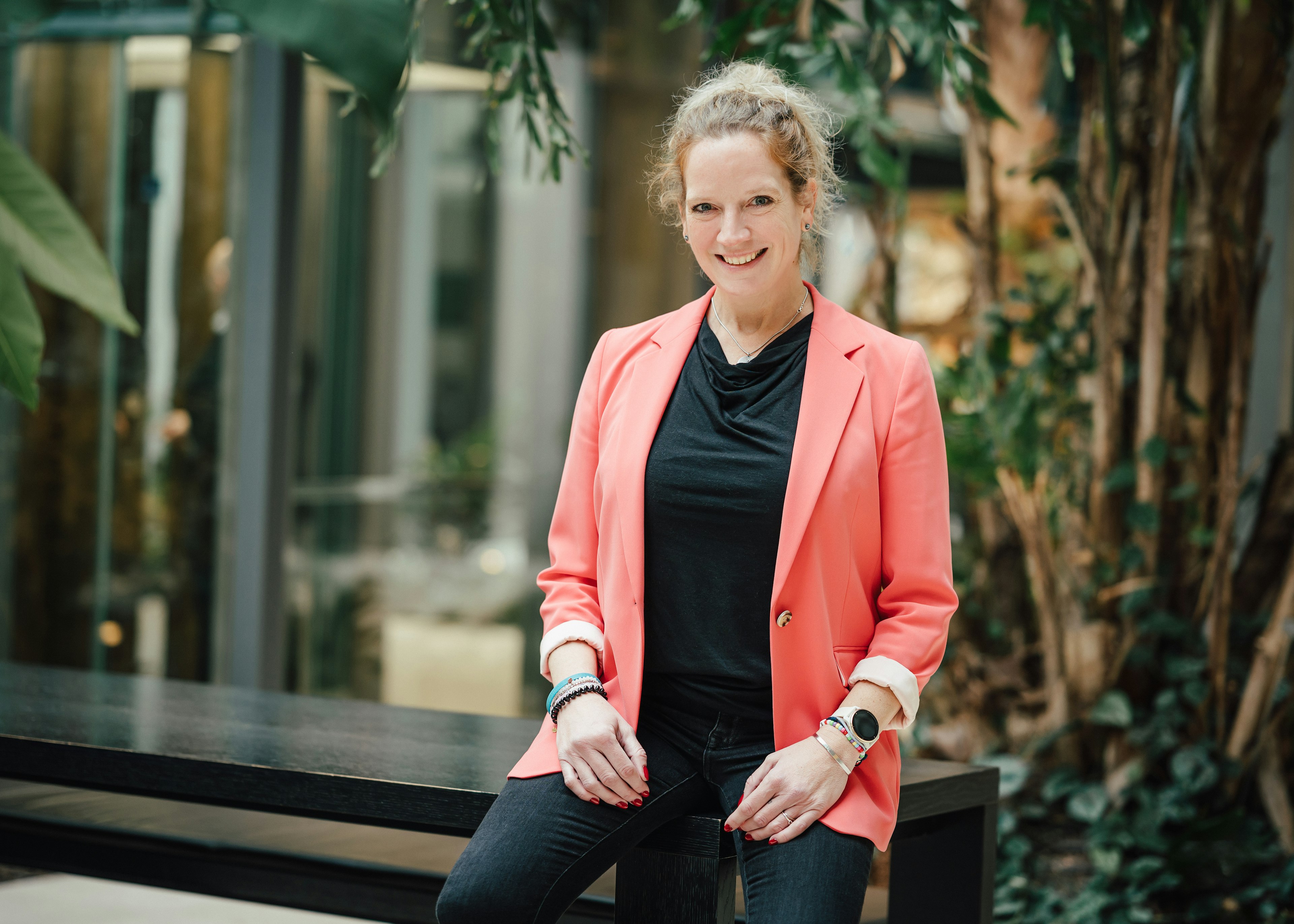 Porträt einer Frau im Business-Outfit, aufgenommen in einem begrünten Innenbereich.