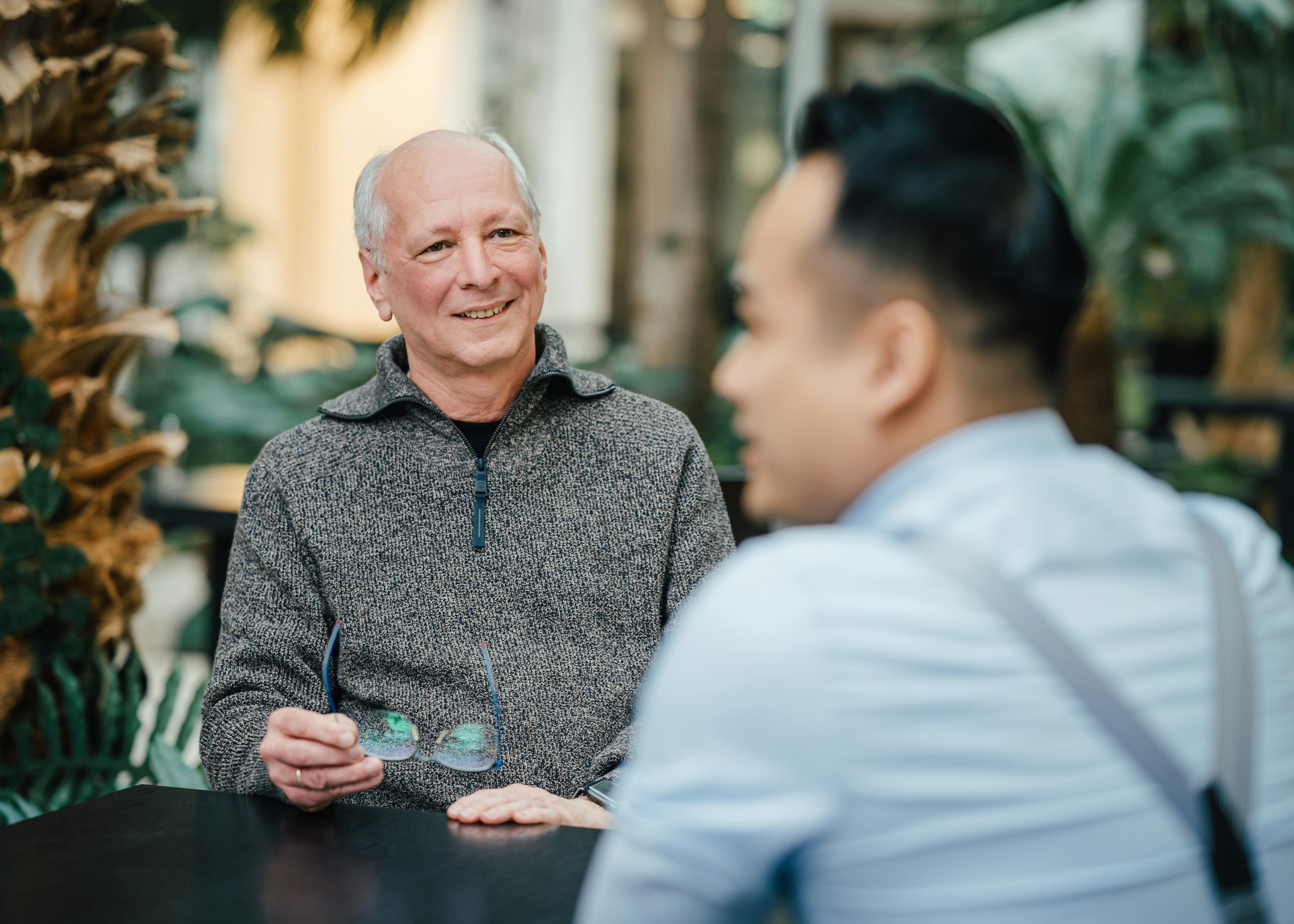 Aufnahme von zwei Männern im Gespräch in einer modernen Umgebung. Der Mann im Vordergrund ist dabei verschwommen abgebildet.