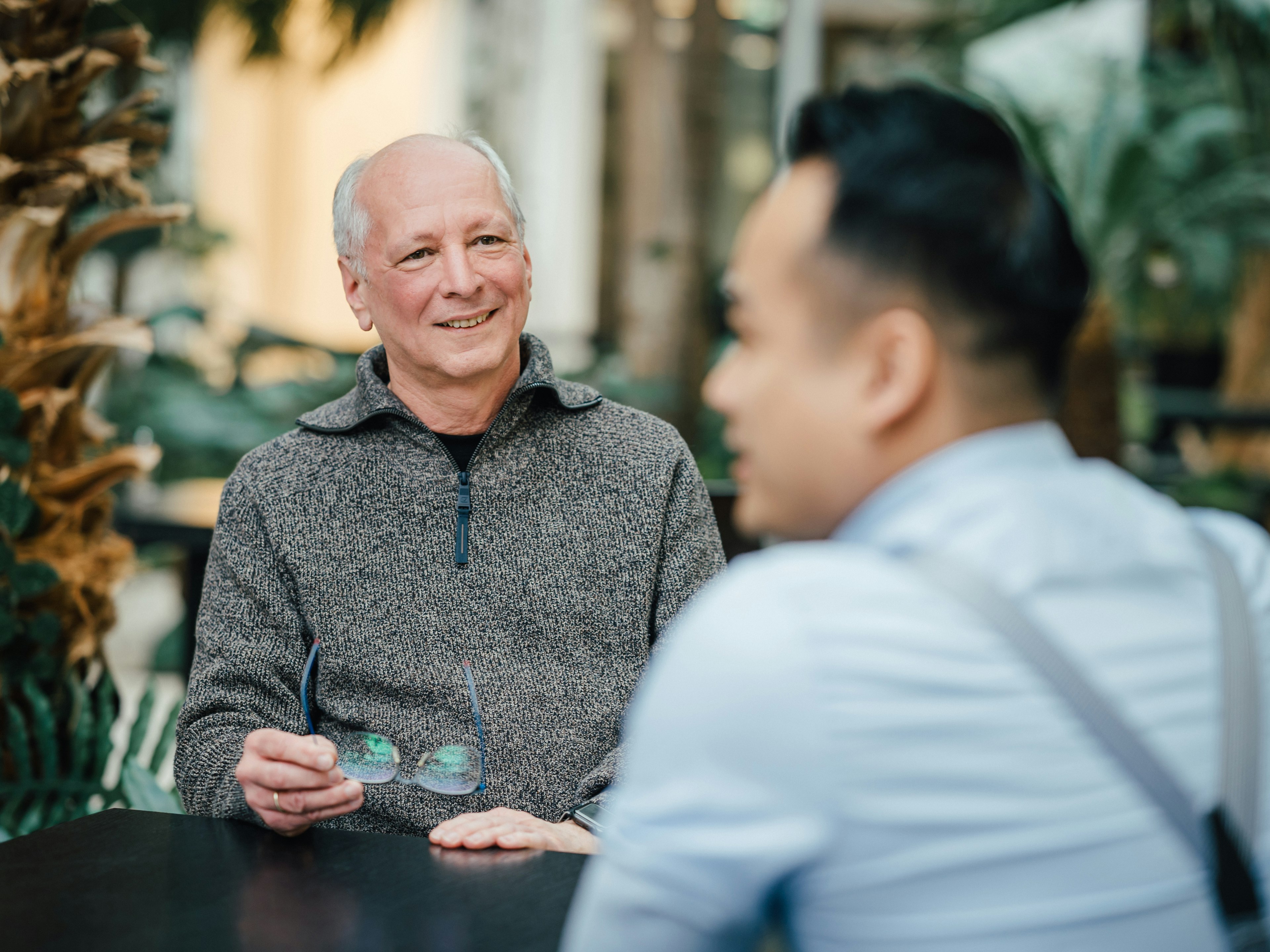 Aufnahme von zwei Männern im Gespräch in einer modernen Umgebung. Der Mann im Vordergrund ist dabei verschwommen abgebildet.