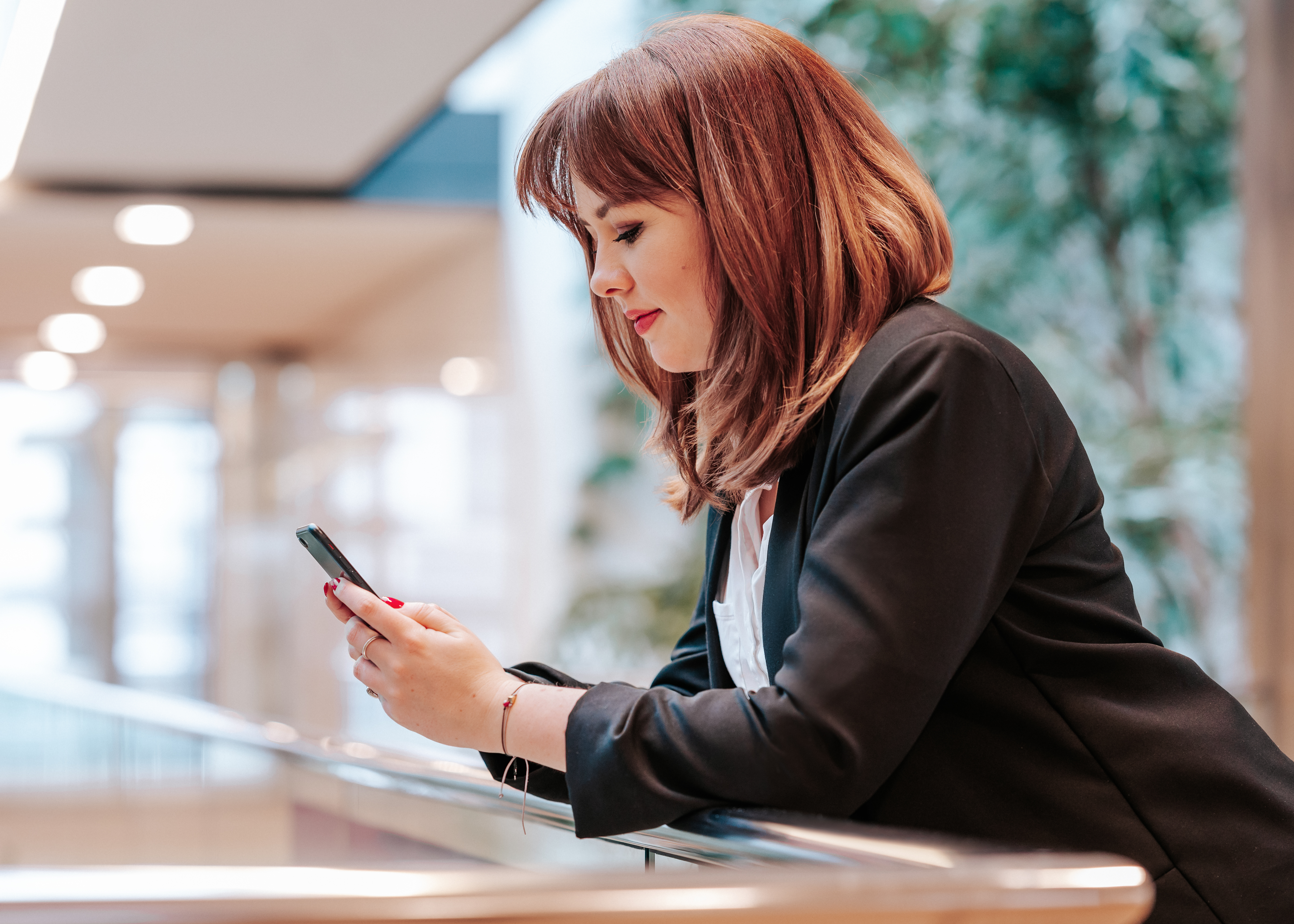 Businessfrau mit Smartphone in der Hand, vertieft in eine Nachricht oder Information, aufgenommen in einer hellen und modernen Büroumgebung.